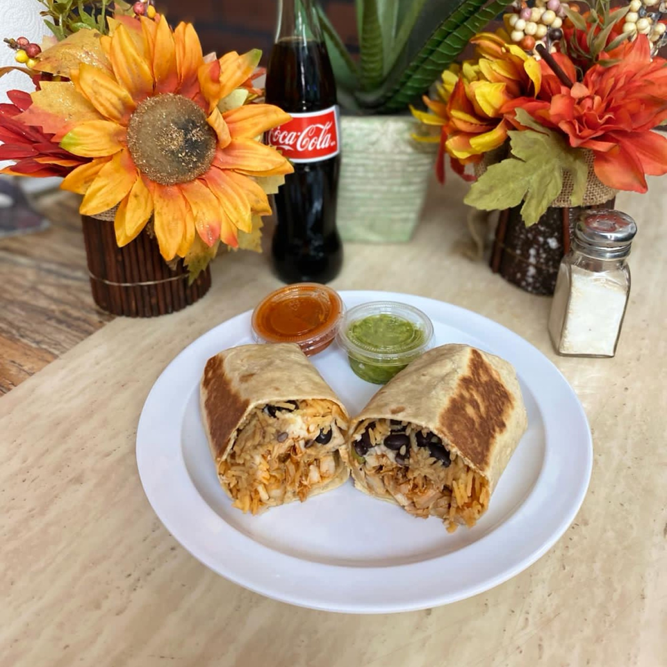 Two burritos cut in half on a white plate with red and green salsa, a Coke, and flowers.