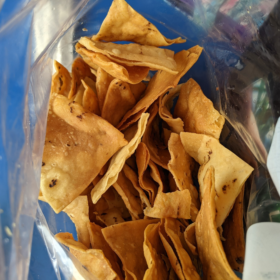 Crispy, golden tortilla chips, some with dark seasoning, inside a clear plastic bag.